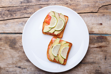 Fresh salmon sandwich with avocado and lime on white plate