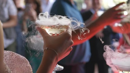 The bride and groom are holding champagne glasses steaming. Dry ice in a glass with champagne in hands of the newlyweds.