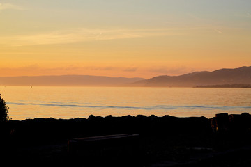 View on lake and mountains scenes through branch of tree in sunset