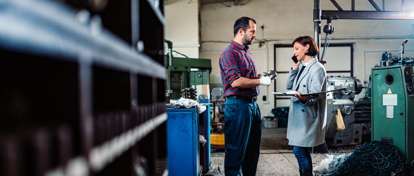 Female engineer standing with machinist and talking on the phone with client