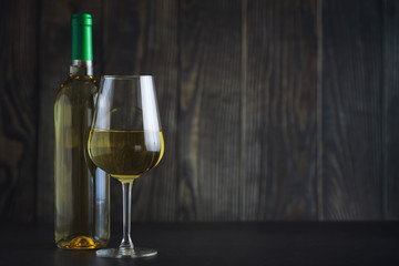 Transparent bottle of white dry wine on the table. White wine glass on a wooden background.