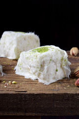Cotton candy with pistachio on wooden board surrounded by nuts against black background