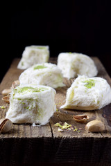 Cotton candy with pistachio on wooden board surrounded by nuts against black background