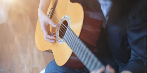 Close-up view of woman playing acoustic guitar in comfortable room