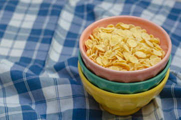 Cornflakes and three bowls of different colors, on a plaid napkin in blue and white. copy space