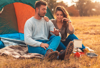 Happy young couple sitting by tent at campsite spending time together in nature.