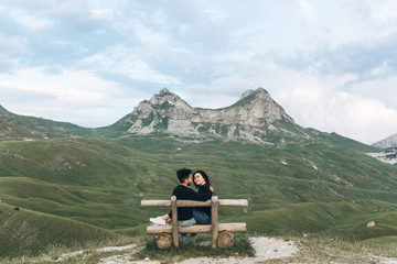 Young couple together on a wooden bench on a background of a mountain landscape in Montenegro.