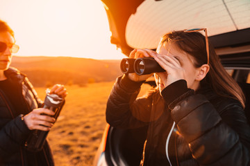 Girl sitting on a car trunk and using binoculars
