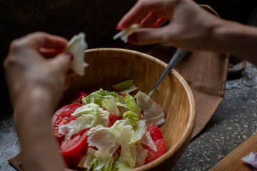 Green vegetable salad in wooden bowl and female hands above it cutting lettuce for finishing dishes. Organic grown plants. Organic cooking series photography