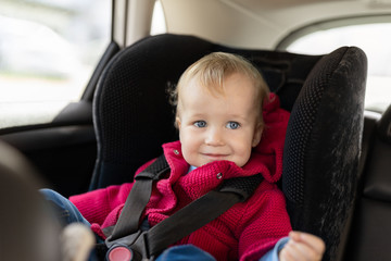 Cute caucasian toodler boy sitting in child safety seat in car during road trip. Adorable baby smiling and enjoying trip in comfortable place in vehicle. Children care and safety on road