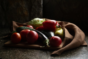 Composition of different vegetables on wooden desk and linen napkins. Still life with organic tomatoes, cucumbers, iceberg lettuce, eggplants and red bell peppers. Organic cooking series photography