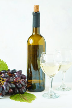 Black grapes, a glass of white wine and a bottle of wine on a light table