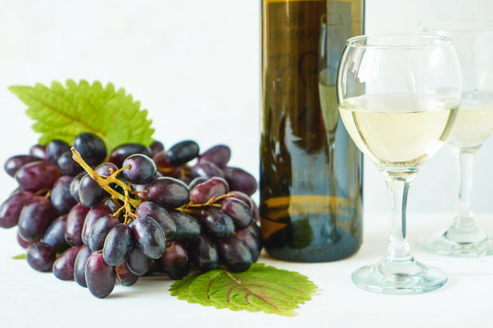 Black grapes, a glass of white wine and a bottle of wine on a light table