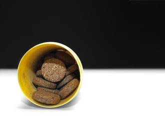 Herbal Supplement Pills in a Yellow Plastic Container on Black and White Background.