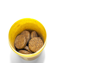Top-Down View of Herbal Supplement Pills in a Yellow Plastic Container on White Background.