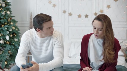 Serious couple looking mobile phones in luxury bedroom.