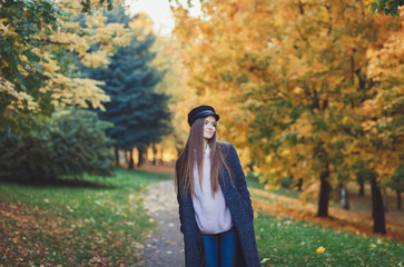 Young woman wearing coat and sweater in the park at sunny autumn day