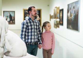 attractive father and daughter regarding paintings in museum