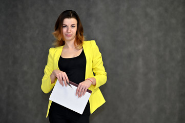 Portrait of a pretty brown-haired young business woman on a gray background in a yellow jacket. He stands in different poses, talking, different emotions.