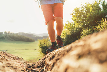 Close up image backpacker traveler feet in trekking boots on mountain dirty path at summertime sunny day.