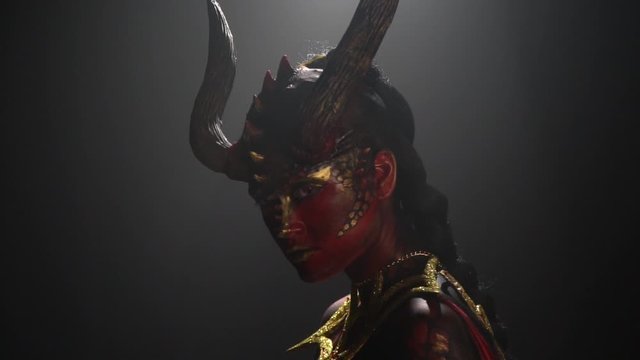 Female devil with horns and red eyes, wearing golden armor is turning around