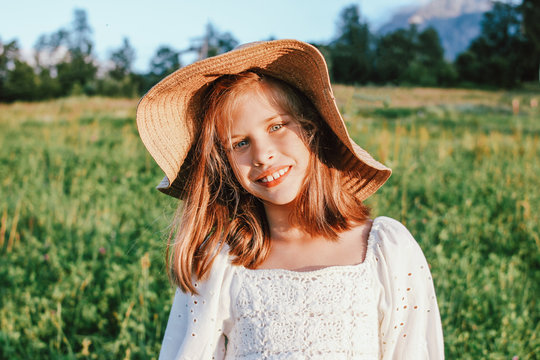 Beautiful romantic preteen girl in straw hat against the background of beautiful houses in mountain, rural scene at sunset