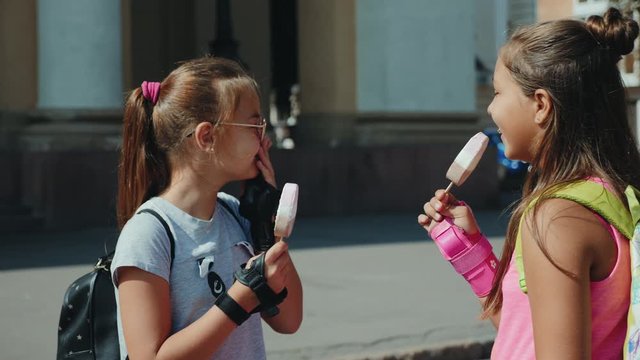 Two teenagers with backpacks eat ice cream in the city square, laugh, talk. The camera is flying around, slow-motion video