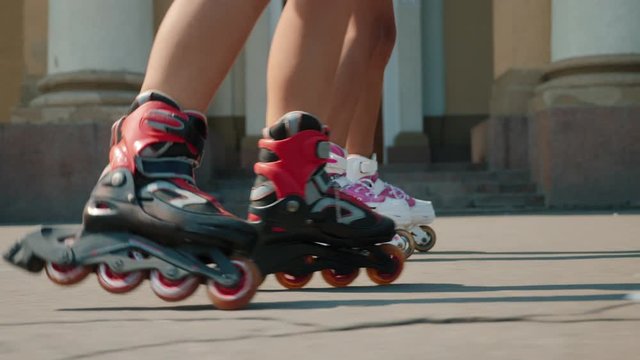 Close-up legs of teenagers riding roller skating down the street. Two girls rollerblading in the town square. Cinematic tracking stabilizer shot, focus on shoes