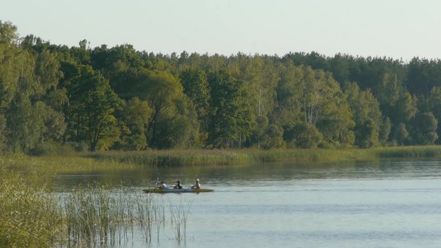 three people on a kayak swim on the lake at sunset and swim to the shore
