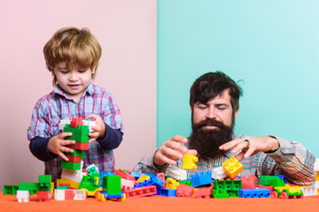 Bearded father and boy play together. Dad and kid build of plastic blocks. Useful toy. Father and son create colorful constructions with bricks. Child care development and upbringing. Father son game