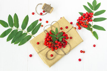 Autumn berries composition. Bunch of rowan (mountain ash) on a white wooden rustic background. Pretty gift box wrapped with brown craft paper and decorated with jute.