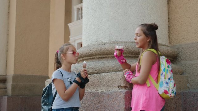 Two girls roller skating eating ice cream and chatting standing near a building in the city. The camera moves in slow motion. Close-up video