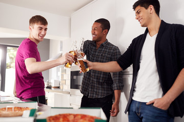 Group Of Male College Students In Shared House Kitchen Drinking Beer And Eating Pizza Together