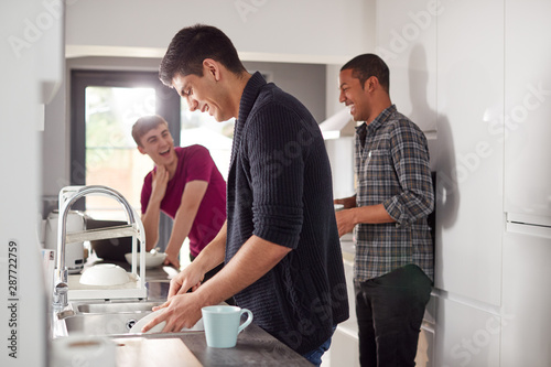 Group Of Male College Students In Shared House Kitchen Washing Up And Hanging Out Together