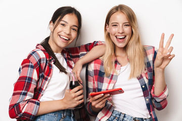 Cheerful happy positive pleased young pretty girls friends sisters posing isolated over white wall background using mobile phone.