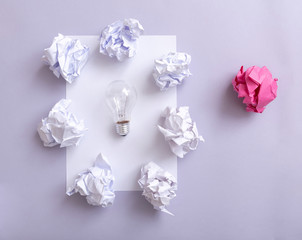 White paper and wastepaper  surrounding a bulb on a violet background.