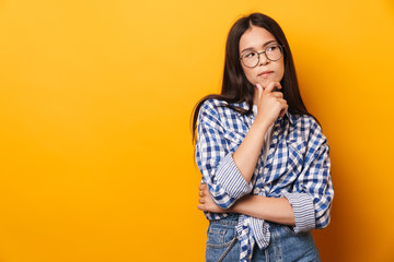 Thoughtful serious young cute teenage girl in glasses posing isolated over yellow wall background.