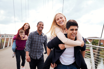 Student Friends With Men Giving Women Piggyback Rides Across City Bridge