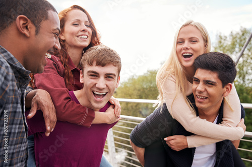 Student Friends With Men Giving Women Piggyback Rides Across City Bridge