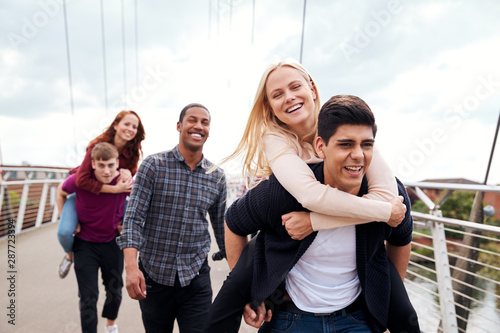 Student Friends With Men Giving Women Piggyback Rides Across City Bridge