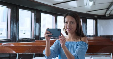 Woman use of smart phone to take photo on mobile phone and sit on star ferry in Hong Kong