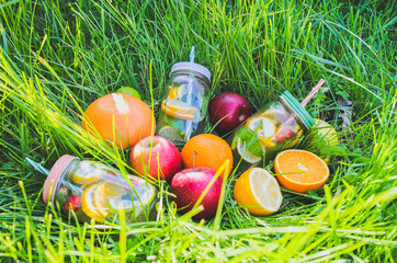 Fresh lemonade in jars with straws. Hipster summer drinks with fruit in green grass outdoors.  Eco-friendly in the nature. Lemons, oranges and berries with mint in the glass. Healthy vegan lifestyle.