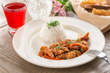 sweet and sour pork stir fried with white rice and red drink on wooden table