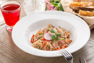 Delicious asian rice noodles with vegetables and bacon and red drink on wooden table