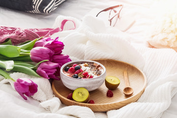 Smoothie bowl and purple tulips on the background on the white bed