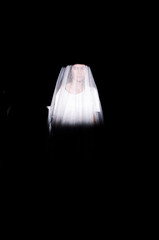 Young woman hidden under a veil is lit in the dim light