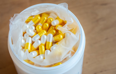 Yellow and white pearl color capsules pill in white drug plastic bottle.