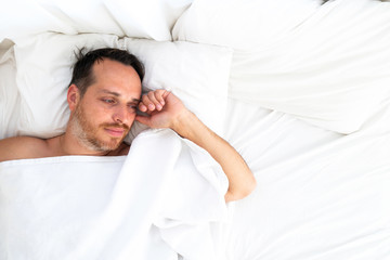 Sad pensive man lying in bed at home alone. Unrequited love concept.