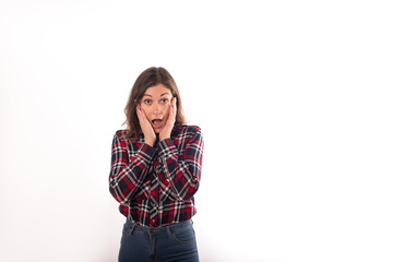 Fototapeta premium Portrait of a frightened hipster girl holds her hands behind the face while standing isolated in studio against white wall background with copy space for promotional content