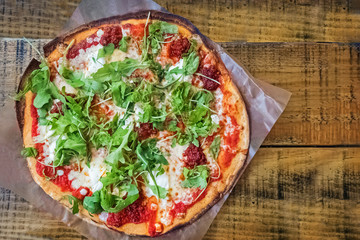 Fresh baked pizza with thin crust, with tomato sause and arugula on wooden table